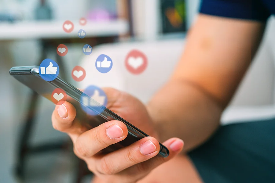 Soziale Medien Likes und Herzen auf einem Smartphone Eine Person hält ein Smartphone in der Hand und sieht sich soziale Medien an. Es werden verschiedene Likes und Herzen angezeigt.