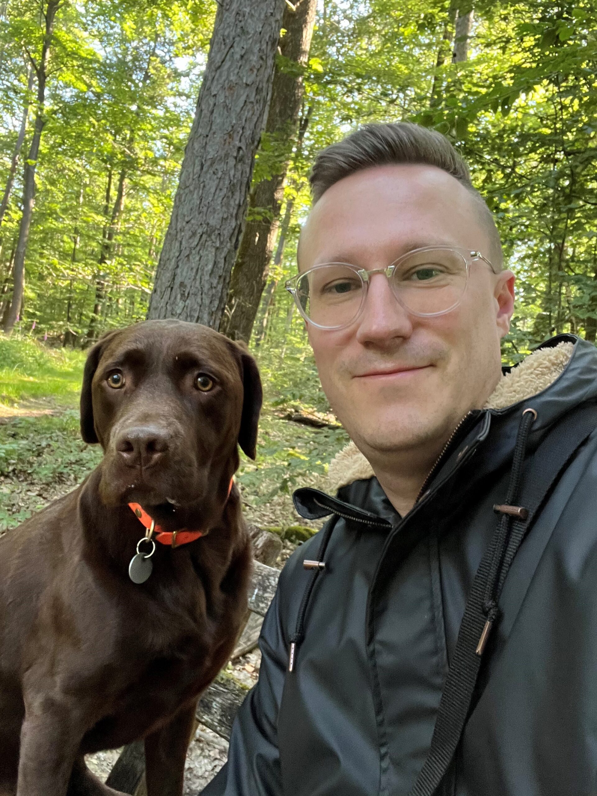 Ein Mann und sein brauner Hund im Wald. Der Hund trägt ein oranges Halsband.