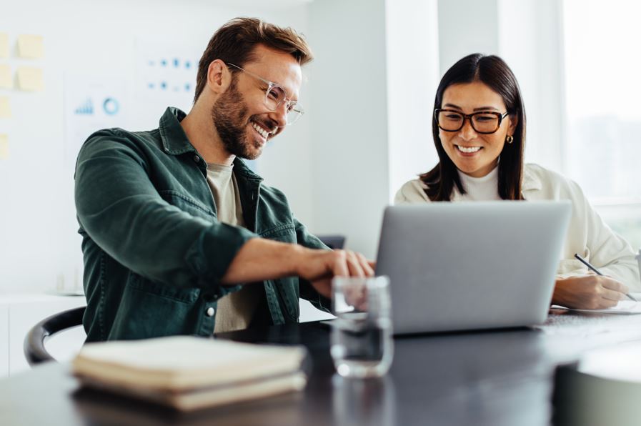 Ein Mann und eine Frau sitzen zusammen und schauen auf einen Laptop. Sie arbeiten gemeinsam an einem Projekt.