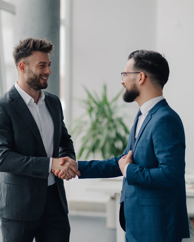 Zwei Männer in Anzügen begrüßen sich. Sie lächeln sich an.