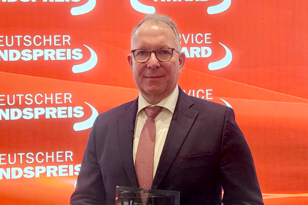 Ein Mann in einem dunklen Anzug und roter Krawatte hält eine Trophäe.