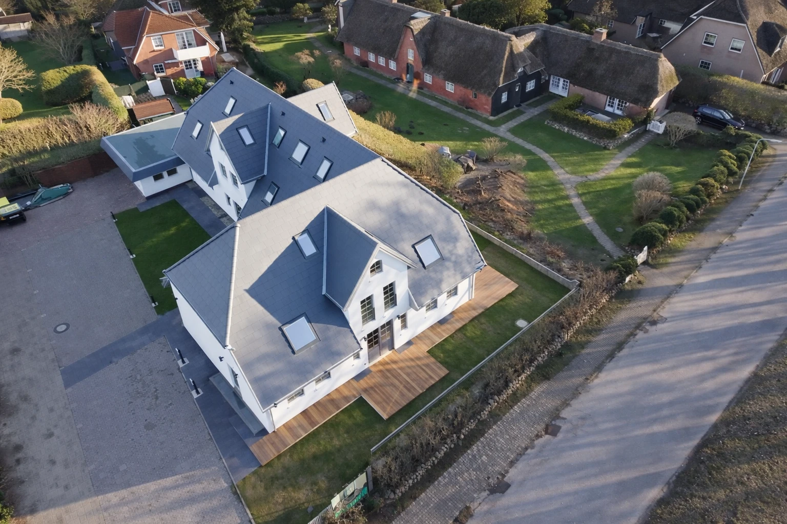 Ein großes weißes Haus mit grauem Dach in einer ruhigen Wohngegend. Das Haus hat mehrere Stockwerke und eine große Terrasse.