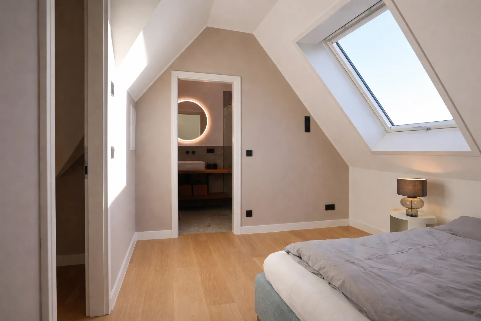 Ein modernes Schlafzimmer mit einer Dachschräge, einem Bett und einem kleinen Bad im Hintergrund. Das Zimmer ist hell und freundlich.