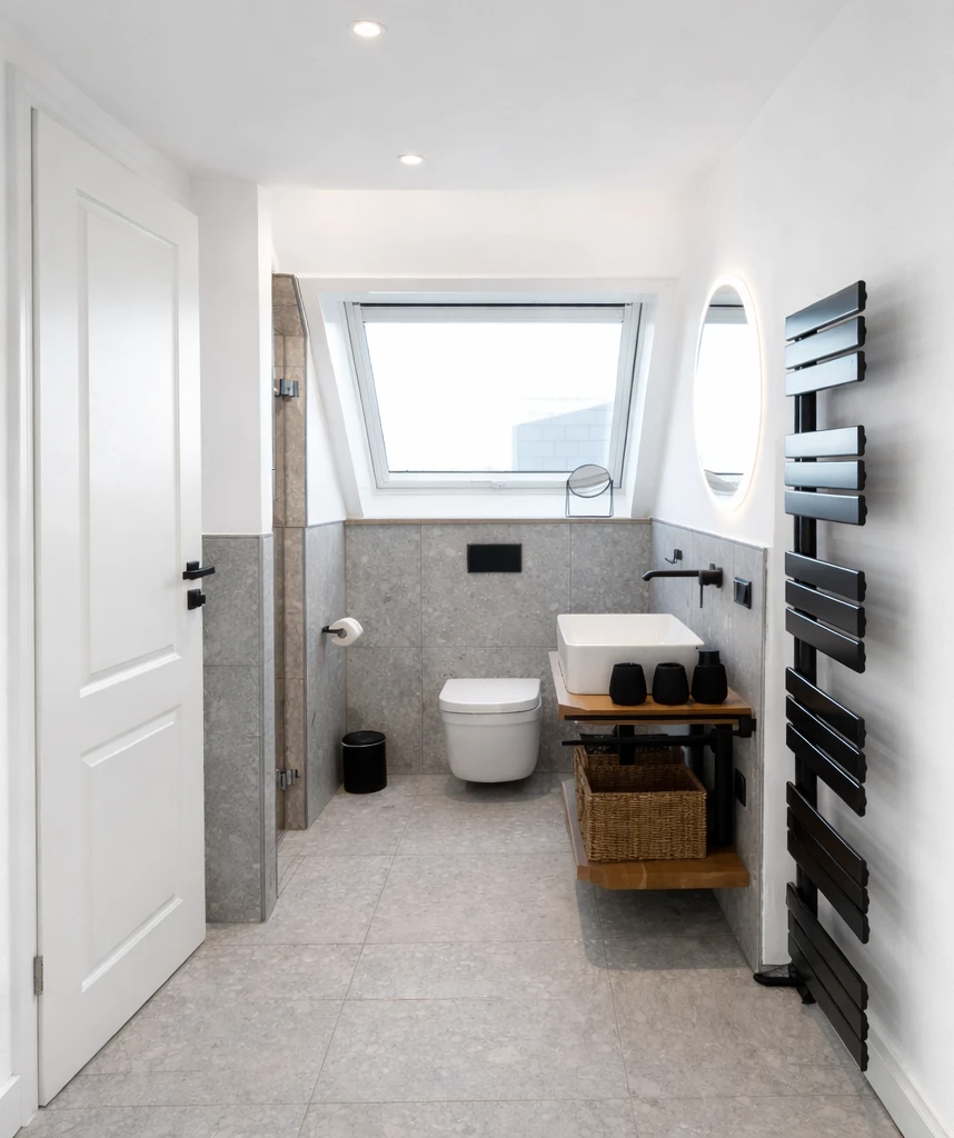 Ein sauberes, hell erleuchtetes Badezimmer mit Toilette, Waschbecken und Dusche. Die Einrichtung ist modern und minimalistisch.