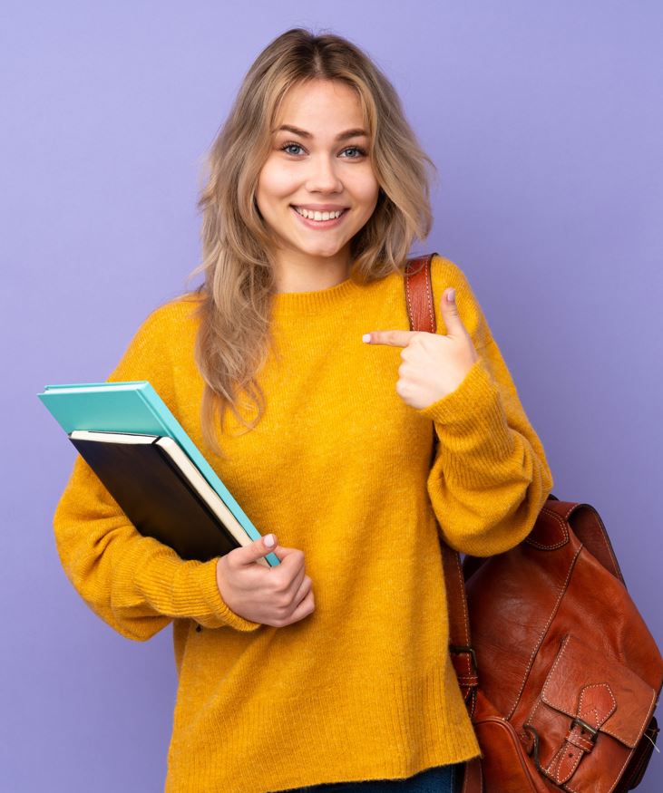 Ein Mädchen hält Bücher und zeigt darauf. Sie trägt eine braune Tasche.