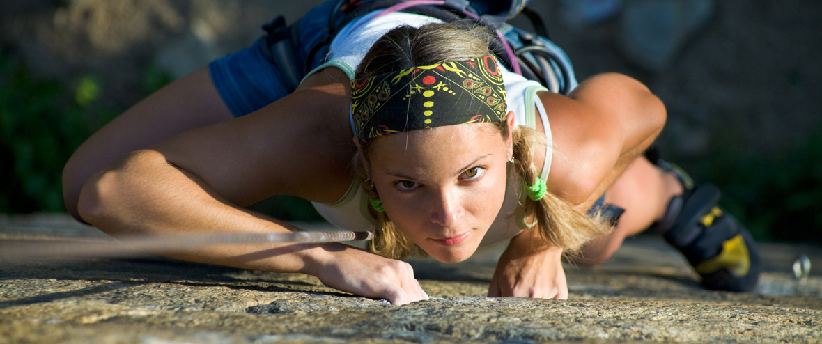 Eine Frau in Sportkleidung klettert an einem Felsen. Sie trägt einen farbenfrohen Kopfschmuck.