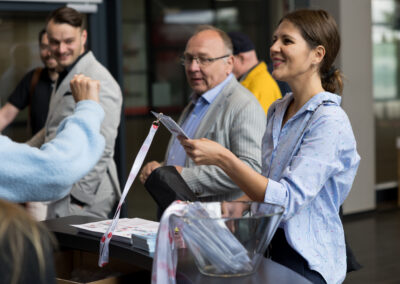 Eine Frau wirft einen Wahlzettel in die Wahlurne. Männer beobachten den Vorgang.