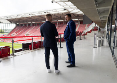 Zwei Männer in blauen Anzügen im Stadion. Sie stehen auf einer Plattform.
