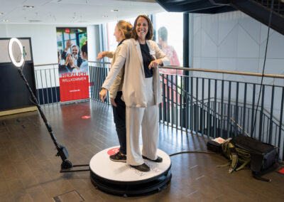 Zwei Frauen in Businesskleidung posieren auf einer runden Plattform. Eine 360-Grad-Fotografie-Ausrüstung ist aufgebaut.