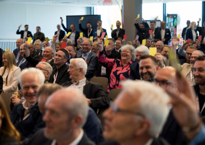 Ein Meer von Gesichtern in einem Konferenzraum. Die Teilnehmer hören aufmerksam zu.