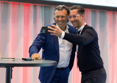 Ein Mann in einem blauen Anzug und ein anderer Mann in einem schwarzen Pullover machen ein Selfie.