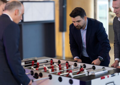 Ein Mann im Anzug spielt Fußball-Tischspiel mit Kollegen