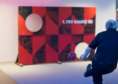 Ein Mann in einem blauen Hemd kickt einen Fußball auf eine Wand mit geometrischen Mustern.