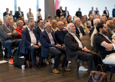 Eine Gruppe von Menschen sitzt in einem Konferenzraum. Die meisten von ihnen sind ältere Herren.