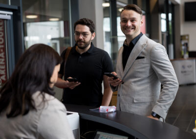 Zwei Männer bezahlen mit ihrem Smartphone an der Kasse. Eine Verkäuferin scannt den Code.