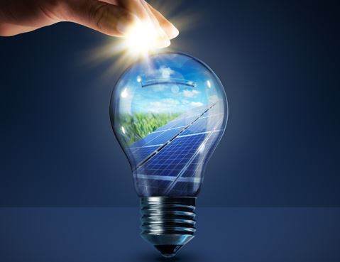 Ein Lichtbulb mit einem Solarpanel im Inneren. Die Hand einer Person berührt die Glühbirne.